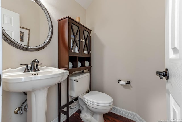 half bath featuring a sink, wood finished floors, toilet, and baseboards