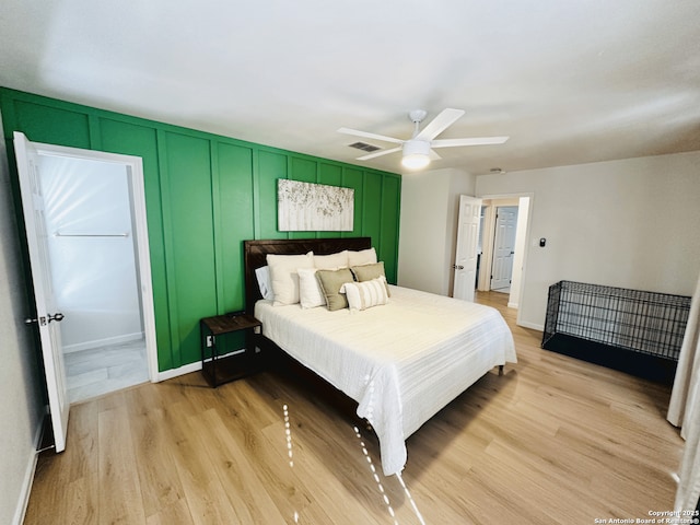 bedroom featuring light wood finished floors, visible vents, baseboards, ceiling fan, and a decorative wall