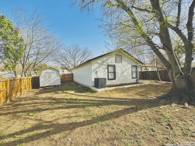 rear view of property featuring a storage shed, central AC unit, an outbuilding, and a fenced backyard