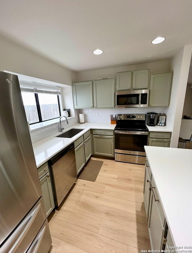 kitchen with decorative backsplash, light wood-style flooring, stainless steel appliances, light countertops, and a sink