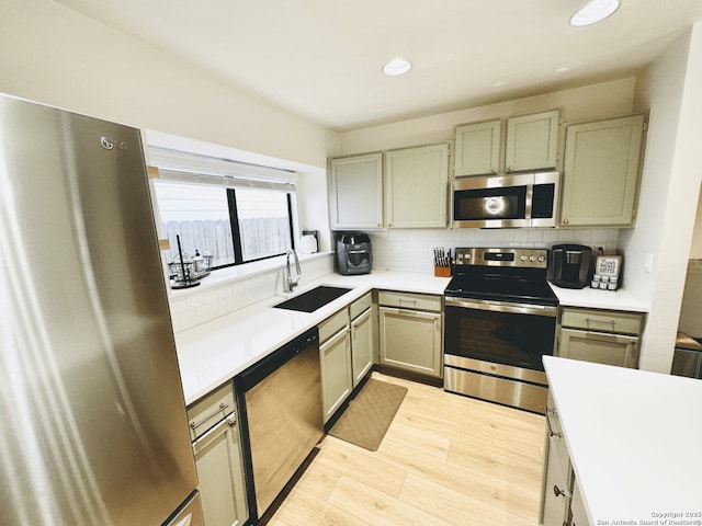 kitchen with light wood-style flooring, a sink, light countertops, appliances with stainless steel finishes, and backsplash