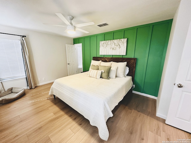 bedroom featuring baseboards, visible vents, a ceiling fan, light wood-style floors, and a decorative wall