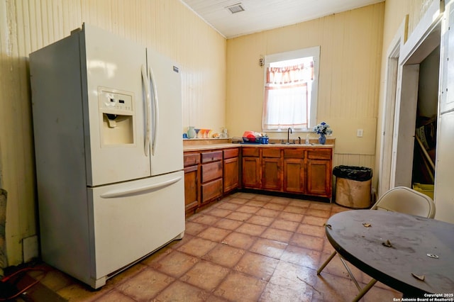 kitchen featuring white refrigerator with ice dispenser, a sink, visible vents, light countertops, and brown cabinetry