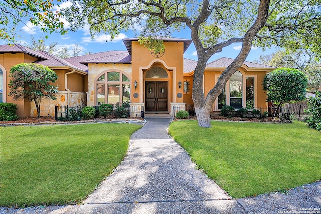 mediterranean / spanish-style home featuring a front lawn, fence, and stucco siding