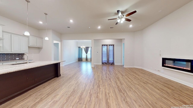 kitchen featuring ceiling fan, light wood-style flooring, a sink, open floor plan, and a glass covered fireplace