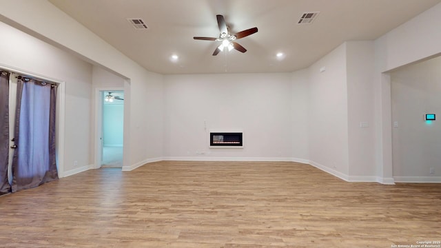 unfurnished living room with light wood-type flooring, a glass covered fireplace, visible vents, and ceiling fan