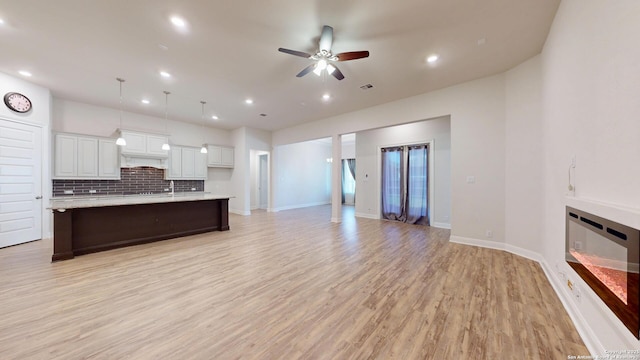 kitchen featuring white cabinets, a ceiling fan, decorative backsplash, light wood-style flooring, and a large island with sink