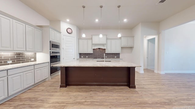 kitchen featuring a kitchen island with sink, light wood-style flooring, a sink, white cabinetry, and stainless steel microwave