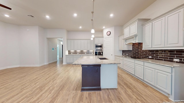 kitchen with black electric stovetop, recessed lighting, white cabinets, light wood-style floors, and a center island with sink