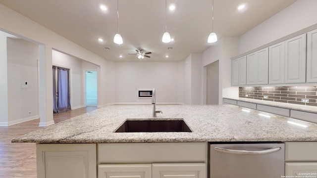 kitchen featuring tasteful backsplash, open floor plan, a sink, light stone countertops, and dishwasher