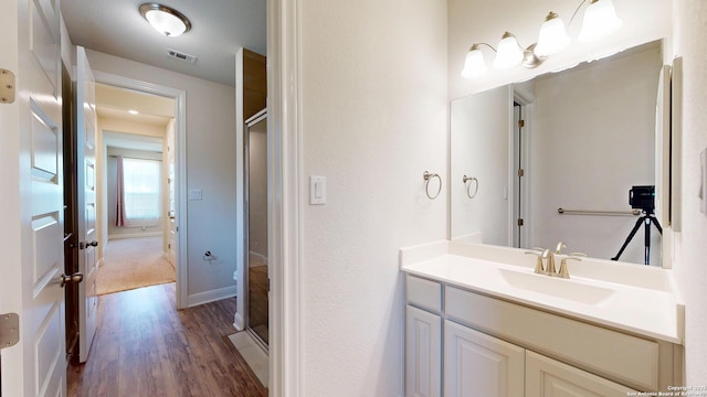 full bath with a stall shower, baseboards, visible vents, wood finished floors, and vanity