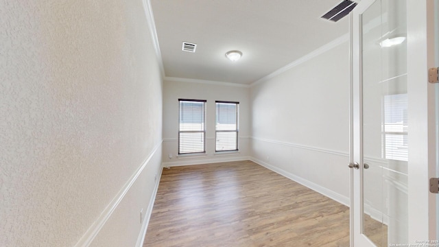 empty room with baseboards, wood finished floors, visible vents, and crown molding