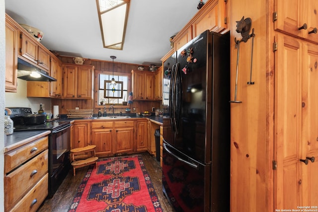 kitchen with brown cabinets, a sink, under cabinet range hood, and black appliances