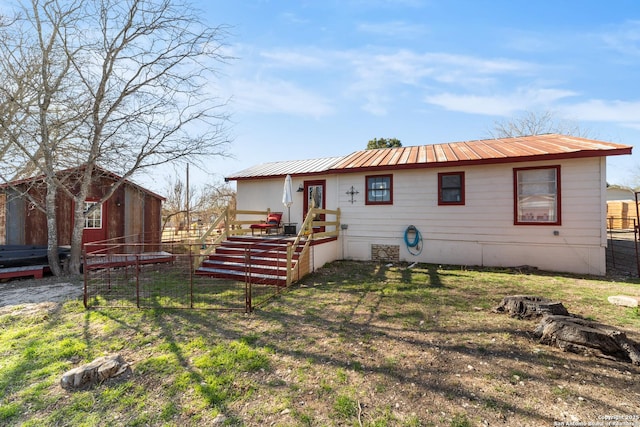 back of house featuring metal roof, fence, an outdoor structure, and a lawn