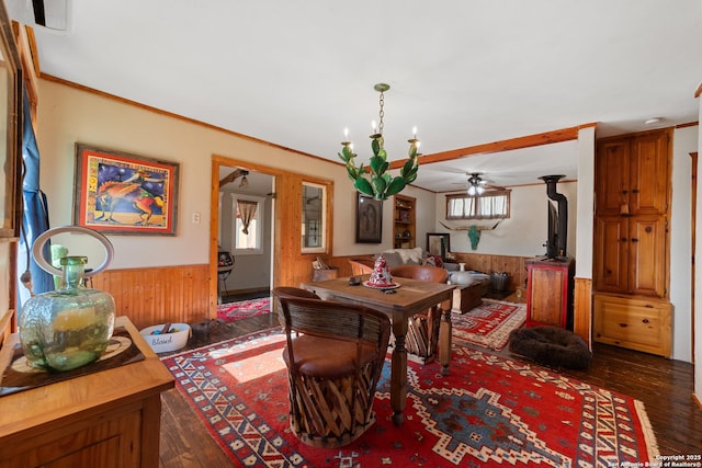 dining space featuring a wainscoted wall, ceiling fan with notable chandelier, dark wood finished floors, and wooden walls