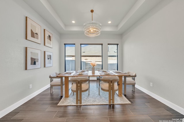 dining space with an inviting chandelier, baseboards, a raised ceiling, and wood finish floors