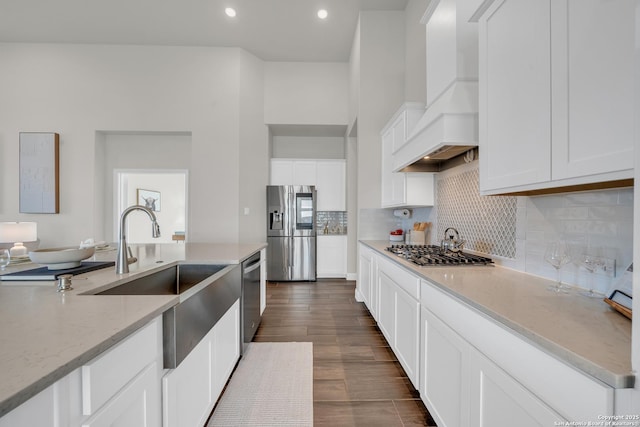 kitchen with light stone counters, stainless steel appliances, premium range hood, a sink, and decorative backsplash