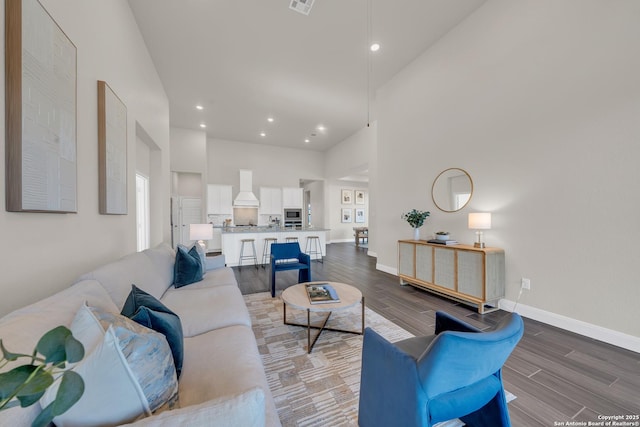 living room featuring a high ceiling, recessed lighting, wood finished floors, and baseboards