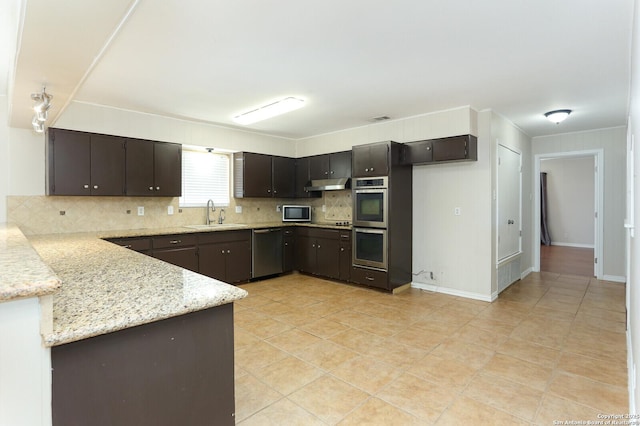 kitchen with dark brown cabinetry, under cabinet range hood, a sink, appliances with stainless steel finishes, and tasteful backsplash