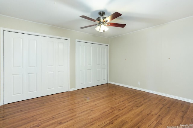 unfurnished bedroom featuring multiple closets, ornamental molding, baseboards, and wood finished floors