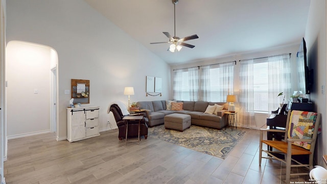 living room featuring arched walkways, high vaulted ceiling, a ceiling fan, baseboards, and light wood-type flooring