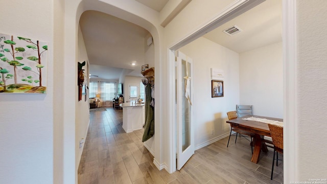 hall with light wood-type flooring, visible vents, arched walkways, and baseboards