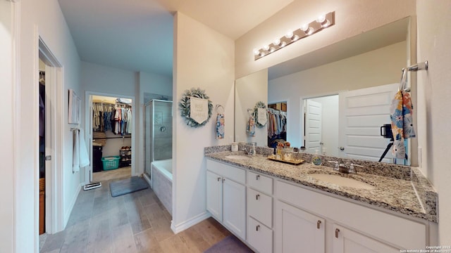 bathroom featuring a walk in closet, tiled shower, a sink, and wood finished floors