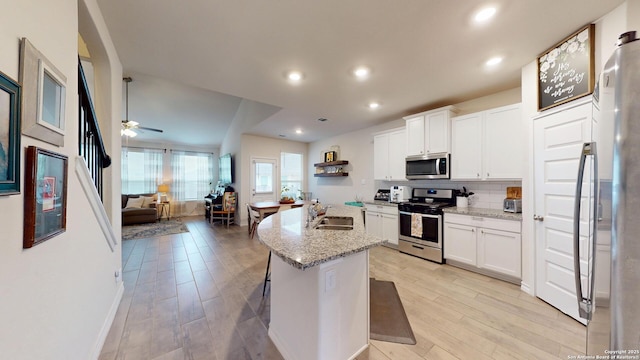 kitchen with stainless steel appliances, open floor plan, white cabinets, and a sink