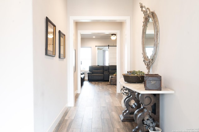 hallway featuring a barn door, wood finished floors, and baseboards