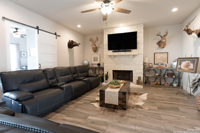 living room featuring a barn door, a stone fireplace, wood finished floors, and a ceiling fan