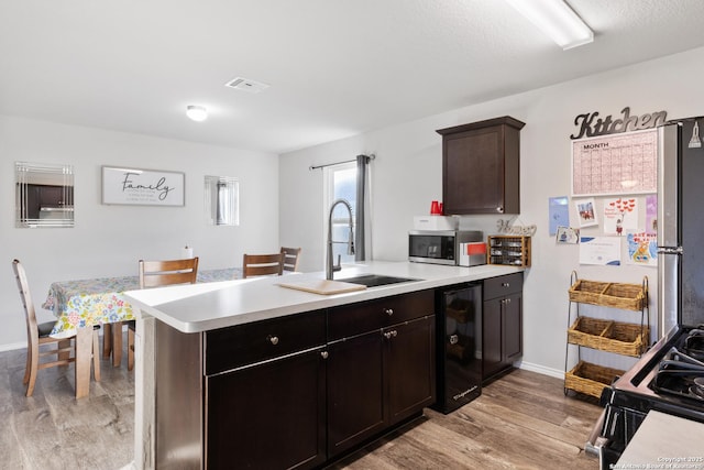 kitchen with wine cooler, stainless steel microwave, a peninsula, light countertops, and gas stove