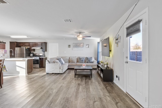 living area featuring light wood-style floors, visible vents, and a ceiling fan