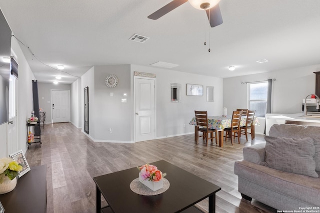 living room with ceiling fan, wood finished floors, visible vents, and baseboards