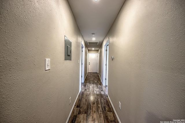 corridor with a textured wall, dark wood-type flooring, visible vents, and baseboards