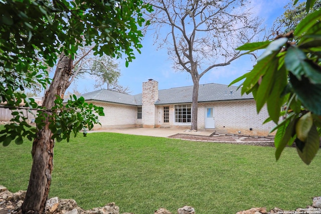 back of property featuring brick siding, a chimney, a shingled roof, a lawn, and a patio area