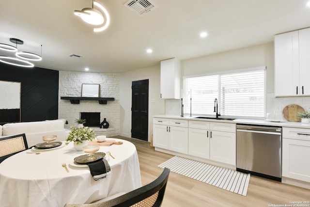 kitchen with dishwasher, light wood finished floors, a sink, and visible vents