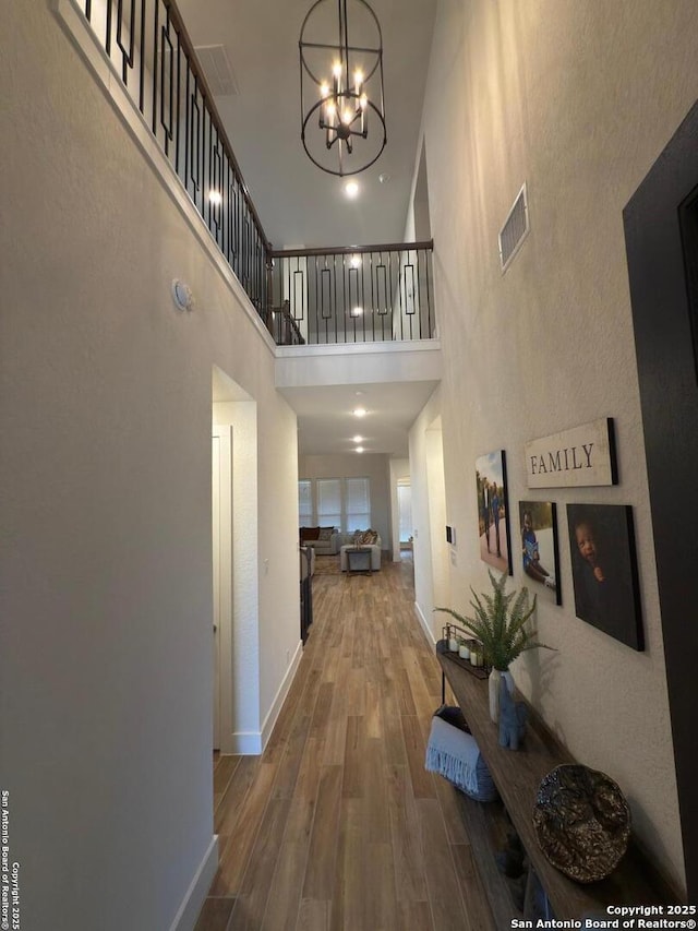 hall with a notable chandelier, wood finished floors, a towering ceiling, baseboards, and visible vents