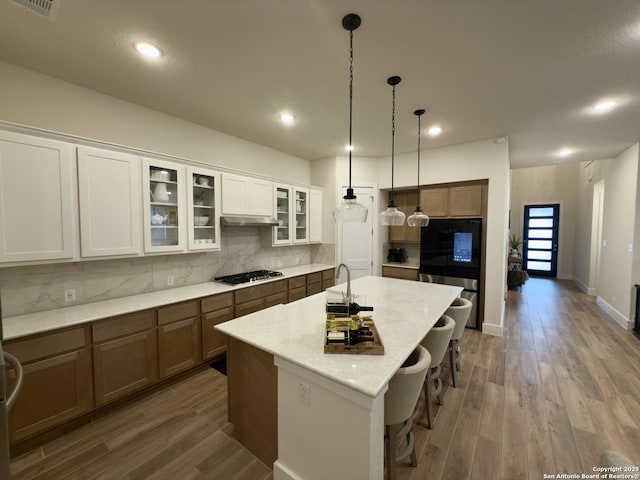 kitchen with pendant lighting, a center island with sink, decorative backsplash, gas cooktop, and wood finished floors