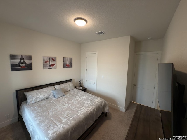 bedroom featuring a textured ceiling, carpet floors, visible vents, and baseboards