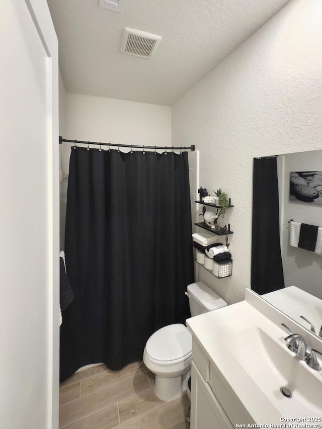 full bathroom with a textured wall, toilet, vanity, visible vents, and wood tiled floor