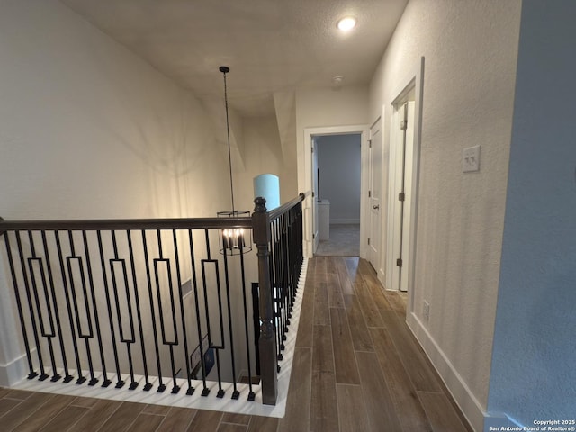 hall featuring an upstairs landing, baseboards, a textured wall, and wood finish floors