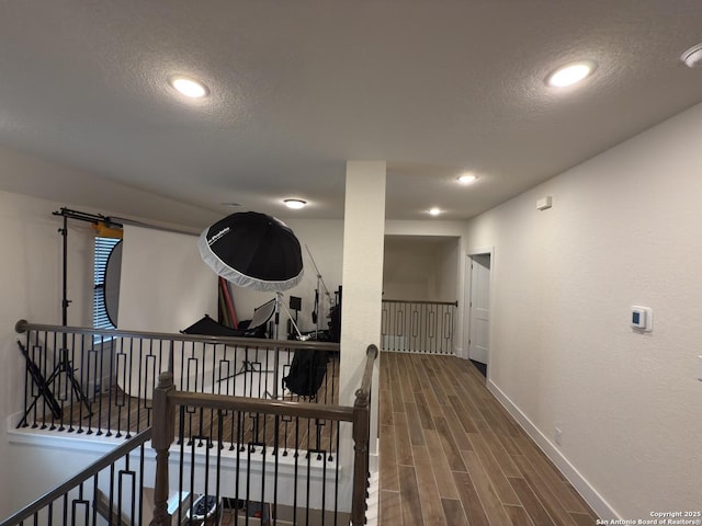 corridor featuring wood finish floors, a textured ceiling, and an upstairs landing