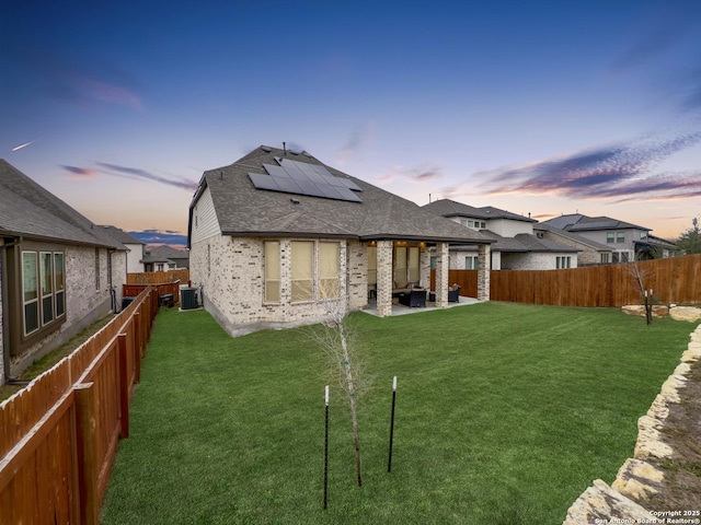 rear view of house with a fenced backyard, solar panels, central AC, and a yard