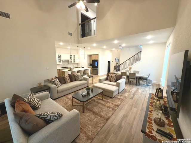 living area with visible vents, light wood-style flooring, stairway, a ceiling fan, and baseboards