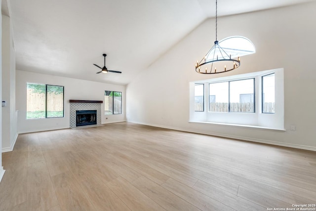 unfurnished living room with high vaulted ceiling, light wood-style flooring, ceiling fan with notable chandelier, a fireplace, and baseboards