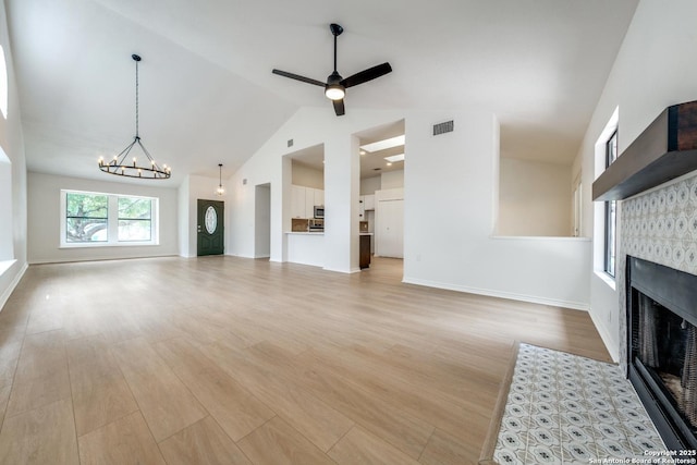 unfurnished living room with baseboards, visible vents, wood finished floors, a fireplace, and ceiling fan with notable chandelier