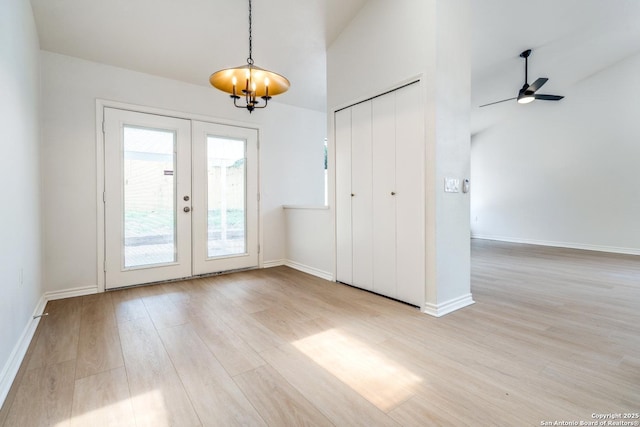 interior space with french doors, baseboards, light wood finished floors, and ceiling fan with notable chandelier