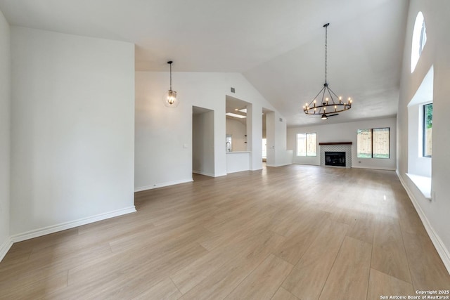 unfurnished living room with baseboards, a tile fireplace, light wood-style flooring, an inviting chandelier, and high vaulted ceiling