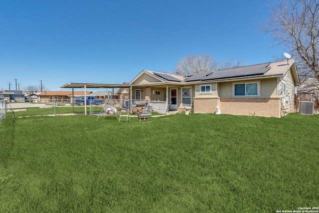 back of house with brick siding, central air condition unit, solar panels, a lawn, and fence