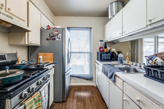 kitchen with dark wood-style flooring, stainless steel appliances, under cabinet range hood, white cabinetry, and a sink